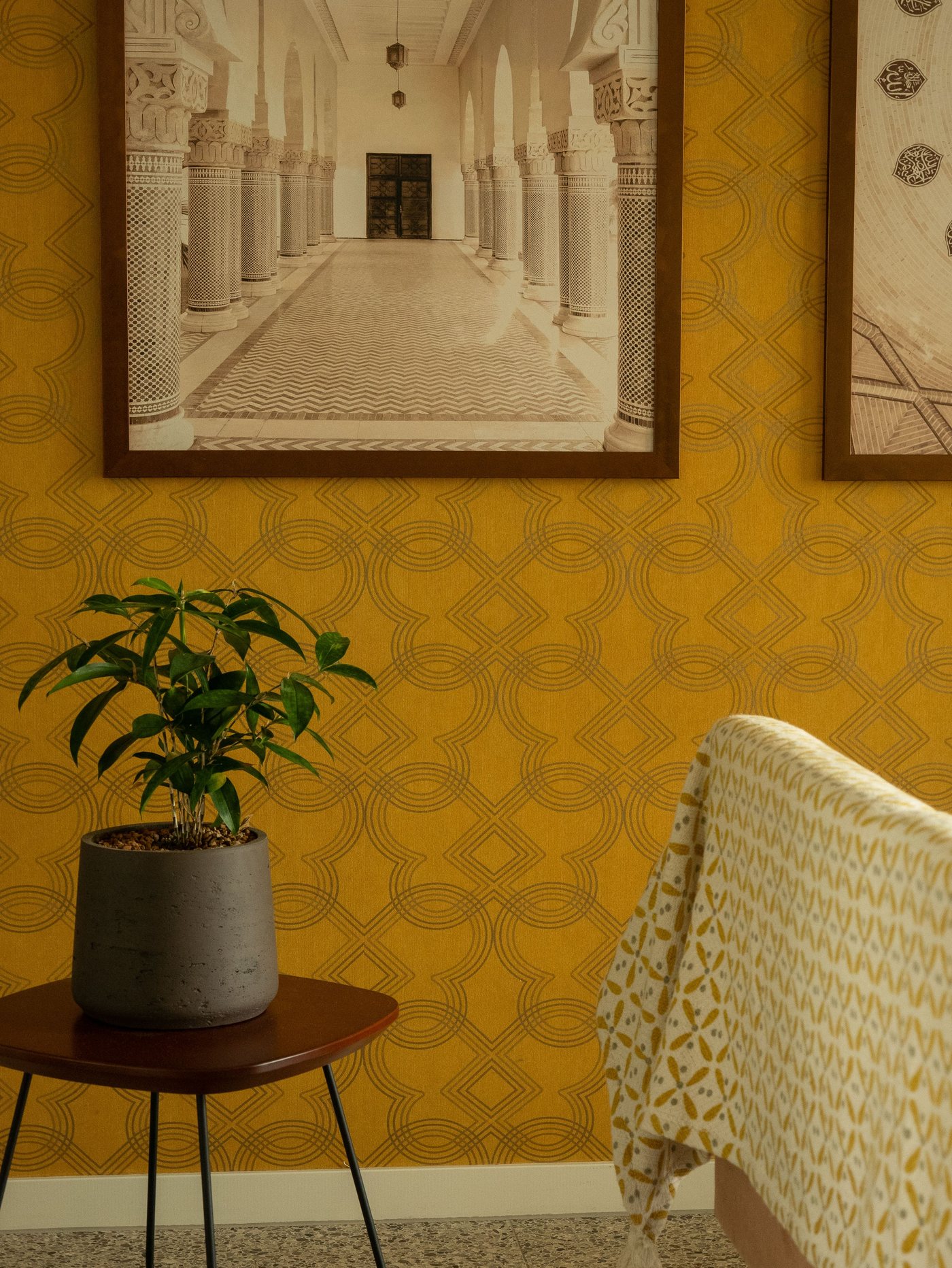 Elegant living room interior finished with a warm gold geometric-pattern wallpaper, framed architectural art, and a potted plant